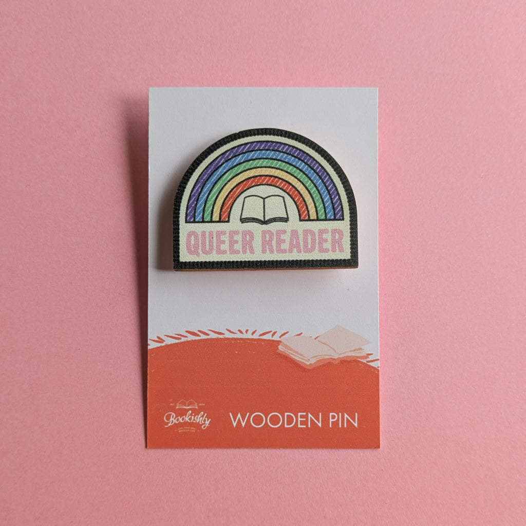 Queer Reader wooden merit badge pin on backing card with pink background