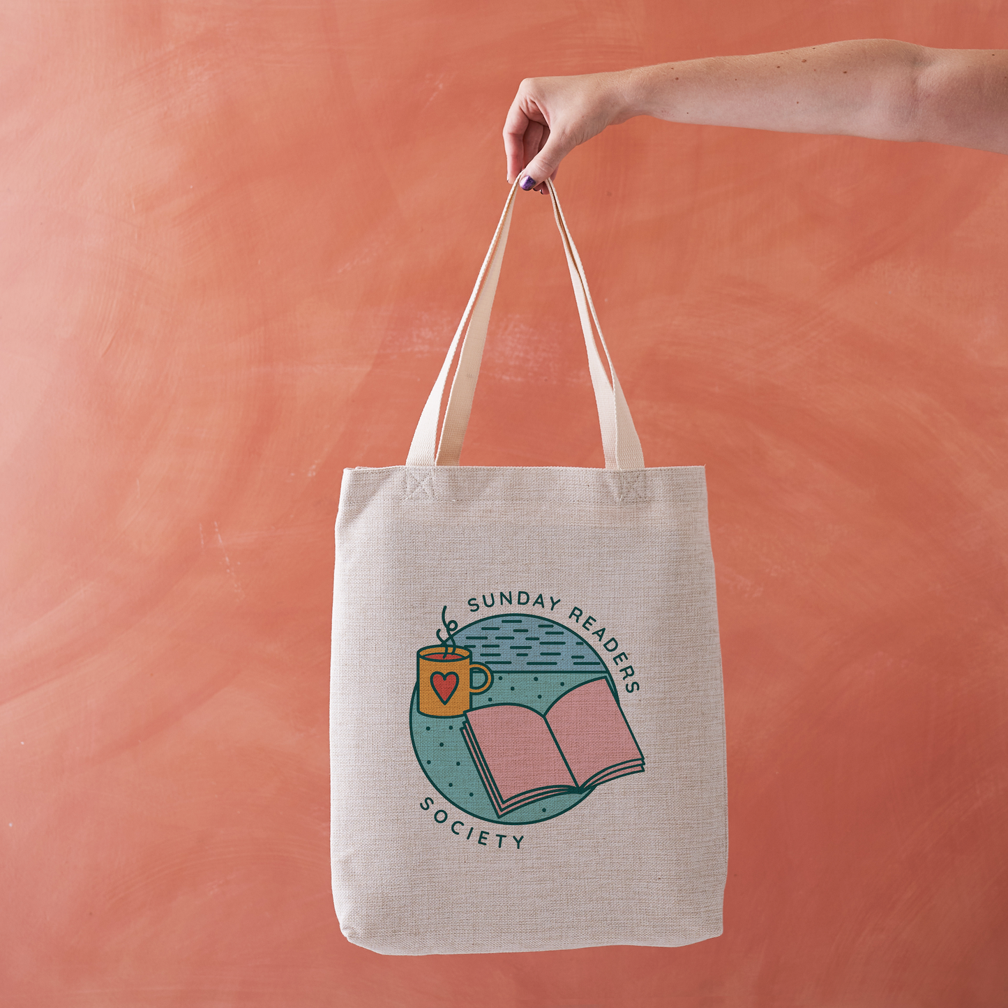 Tote bag with “Sunday Readers Society” design featuring open book and mug illustration.