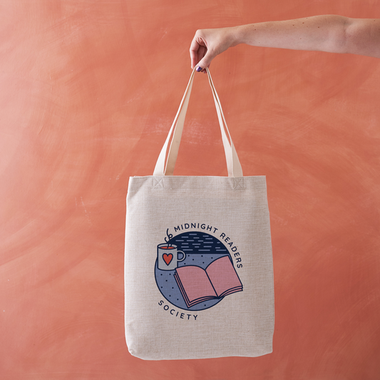 Tote bag with “Midnight Readers Society” design featuring book, mug, and night sky illustration.