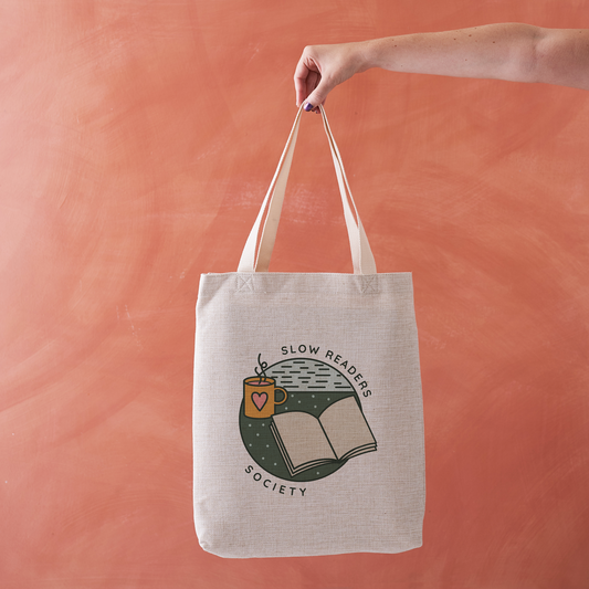 Tote bag with “Slow Readers Society” design featuring open book and mug illustration.